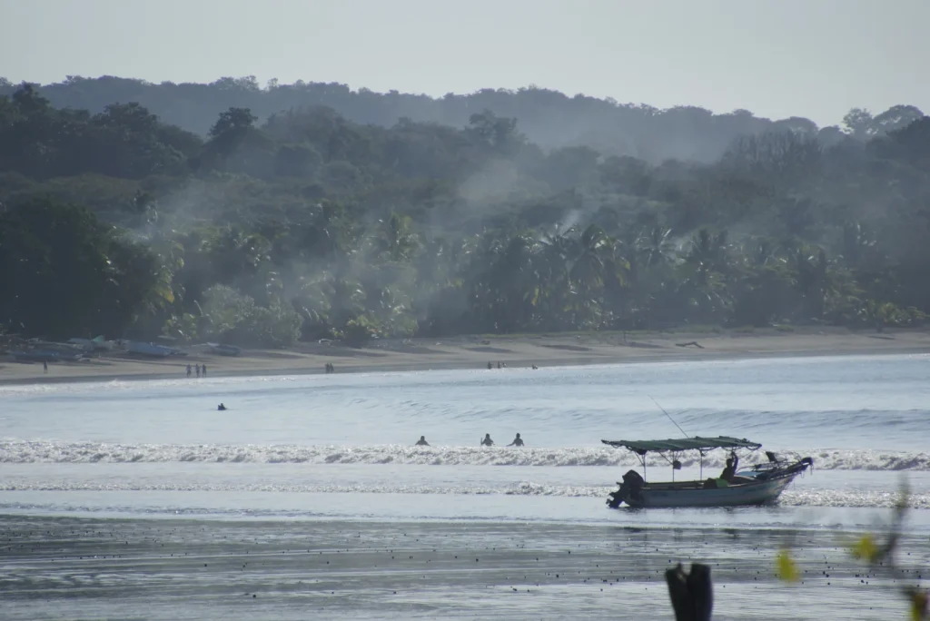 A small boat in Sámara bay with a palm-lined beach and forested hills behind it